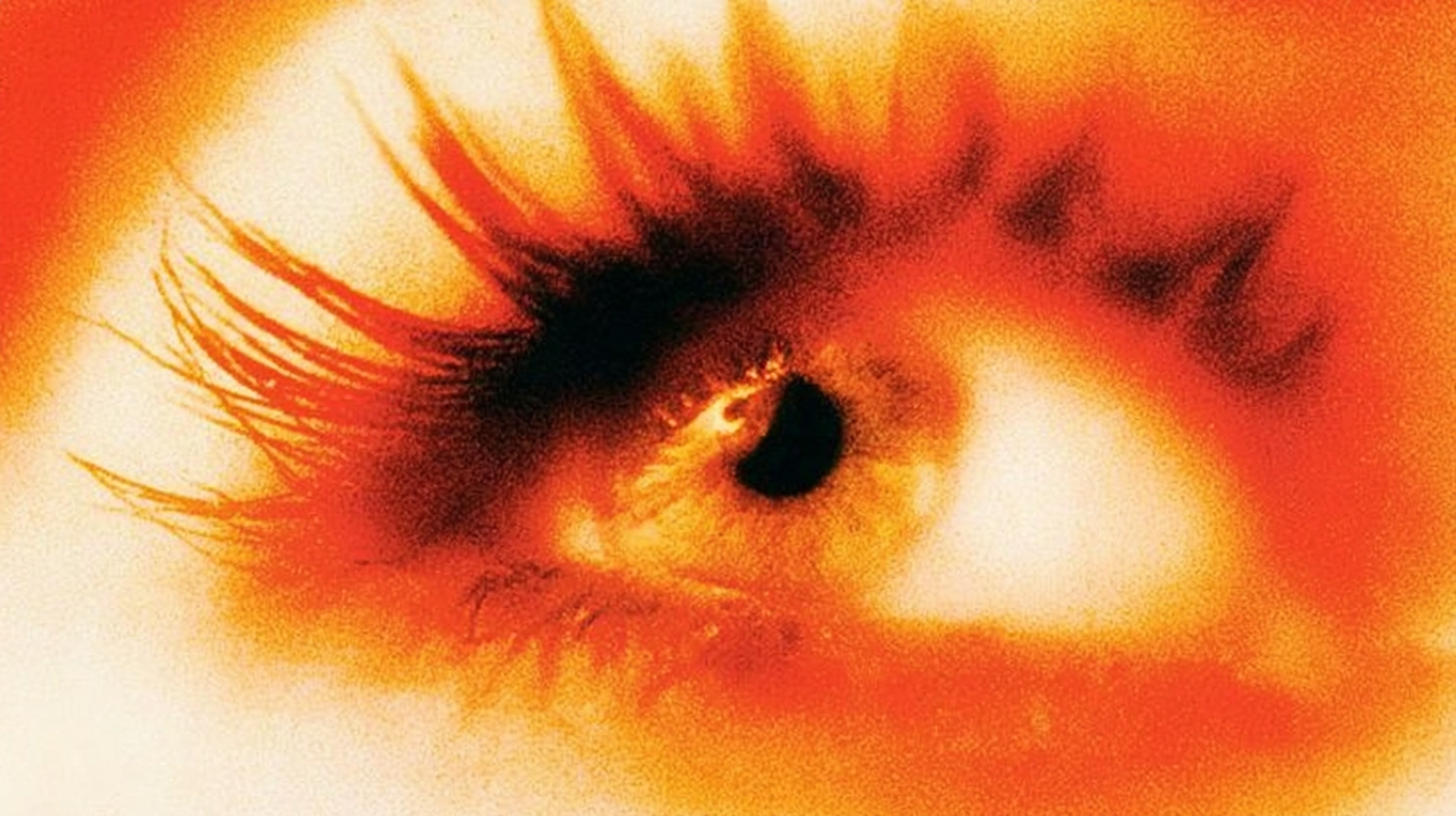 Primer plano artístico de un ojo humano con iris dorado y pupila negra, rodeado de un resplandor intenso en tonos naranjas